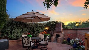 Un patio al aire libre con chimenea de ladrillo, una mesa con sillas y un paraguas grande.