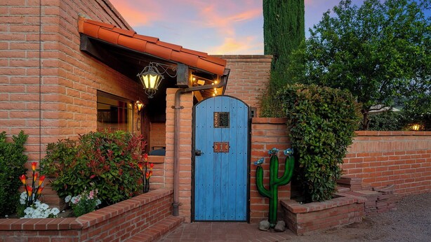 Un edificio de ladrillo con una puerta azul, un lámpara colgante y una planta de cactus.