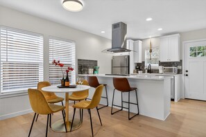 Uma cozinha moderna com ilha central, armários brancos e coifa de aço inoxidável.