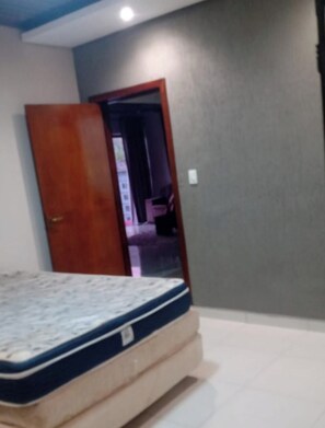 Un dormitorio con una cama, una puerta de madera y una pared gris.