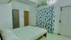 A bedroom with a single bed, an air conditioning unit, a ceiling fan, a door, and a curtain with a floral pattern.