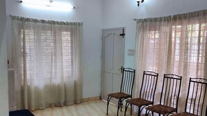 A room with a bed, four chairs, a ceiling fan, and a door.