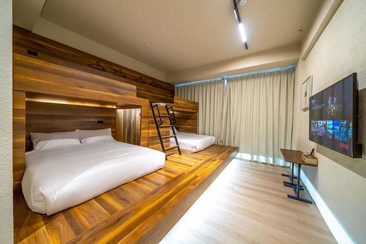 Una habitación de hotel moderna con una pared de acento de madera, una cama, un escritorio con silla, un televisor montado en la pared y una ventana con cortinas.