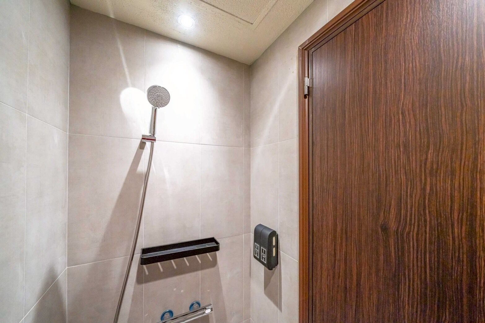 A shower area with a handheld showerhead, a towel rack, and a soap dispenser.