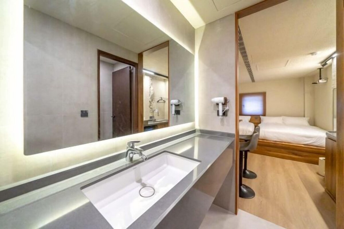 Un baño moderno con un espejo grande, un lavamanos blanco y una zona de ducha.