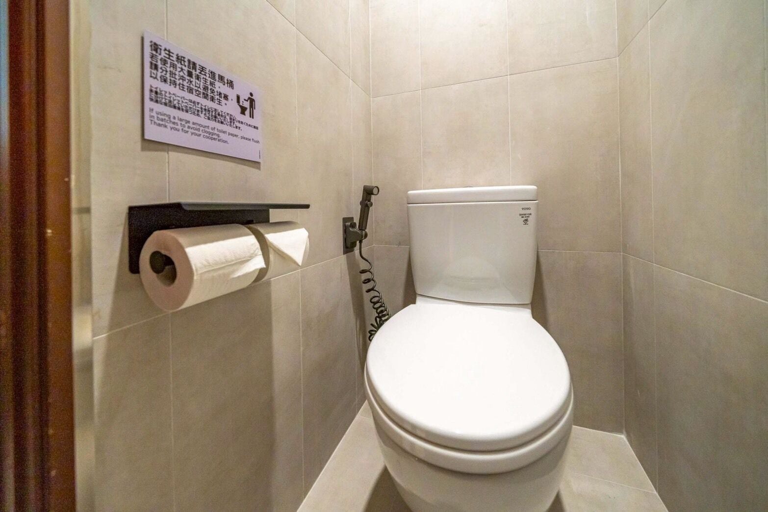 A small, clean bathroom with a toilet, a toilet paper holder, and a sign on the wall.