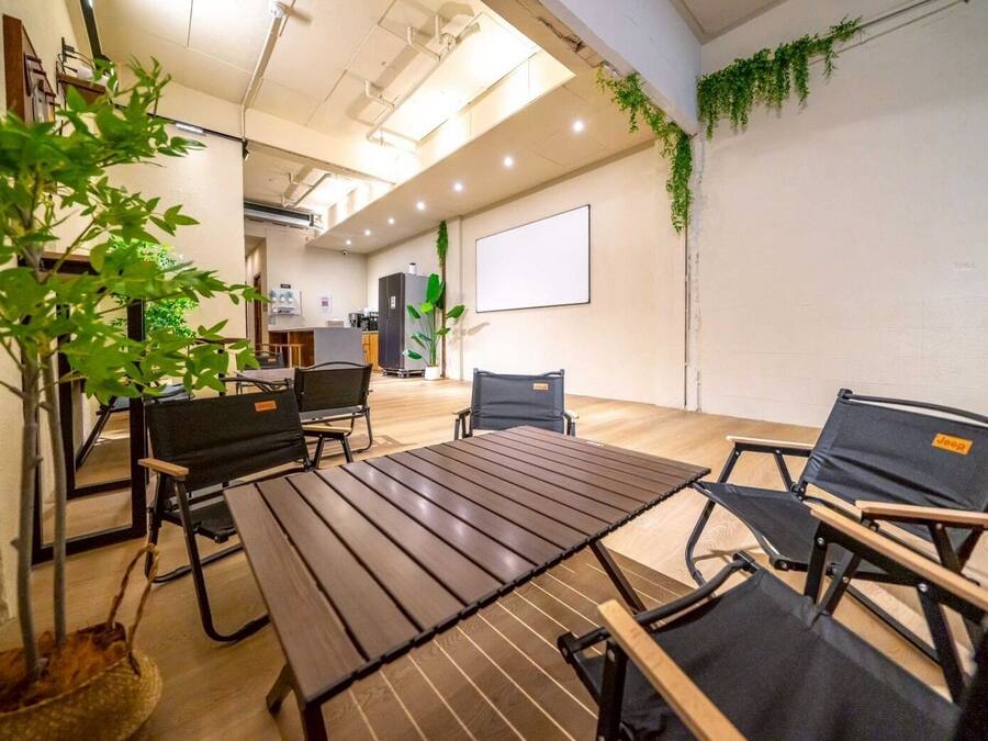 A modern meeting room with a wooden table, black chairs, and a projector screen.