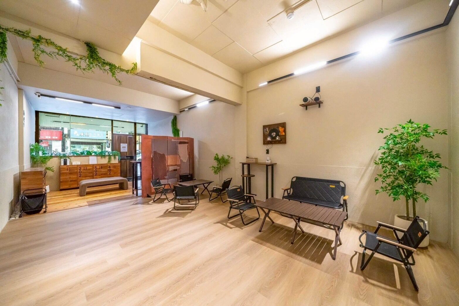 A spacious lobby with a wooden floor, a reception desk, a seating area with a bench and chairs, and a large window offering a view of the street.