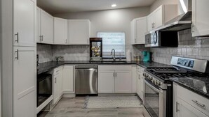 A modern kitchen with white cabinets, stainless steel appliances, and a black countertop. - Vibrant Fiesta-Style Retreat (San Antonio)