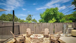 A backyard with a stone patio, a circular fire pit, and four Adirondack chairs. - Vibrant Fiesta-Style Retreat (San Antonio)