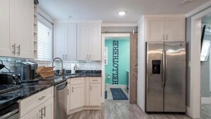 Una cocina moderna con armarios blancos, un refrigerador de acero inoxidable y una encimera negra.