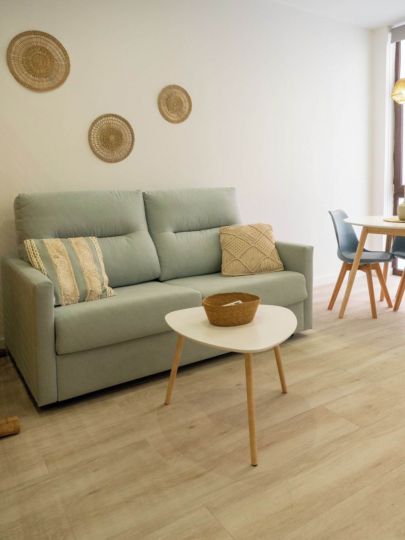 Una sala de estar con un sofá verde claro, una mesa de centro redonda y un comedor con una mesa y sillas de madera.