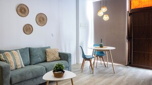 A modern living room with a green sofa, a round coffee table, and a dining table with chairs. There are wall decorations and a wooden door in the background. - Boho Beach Flats (València)