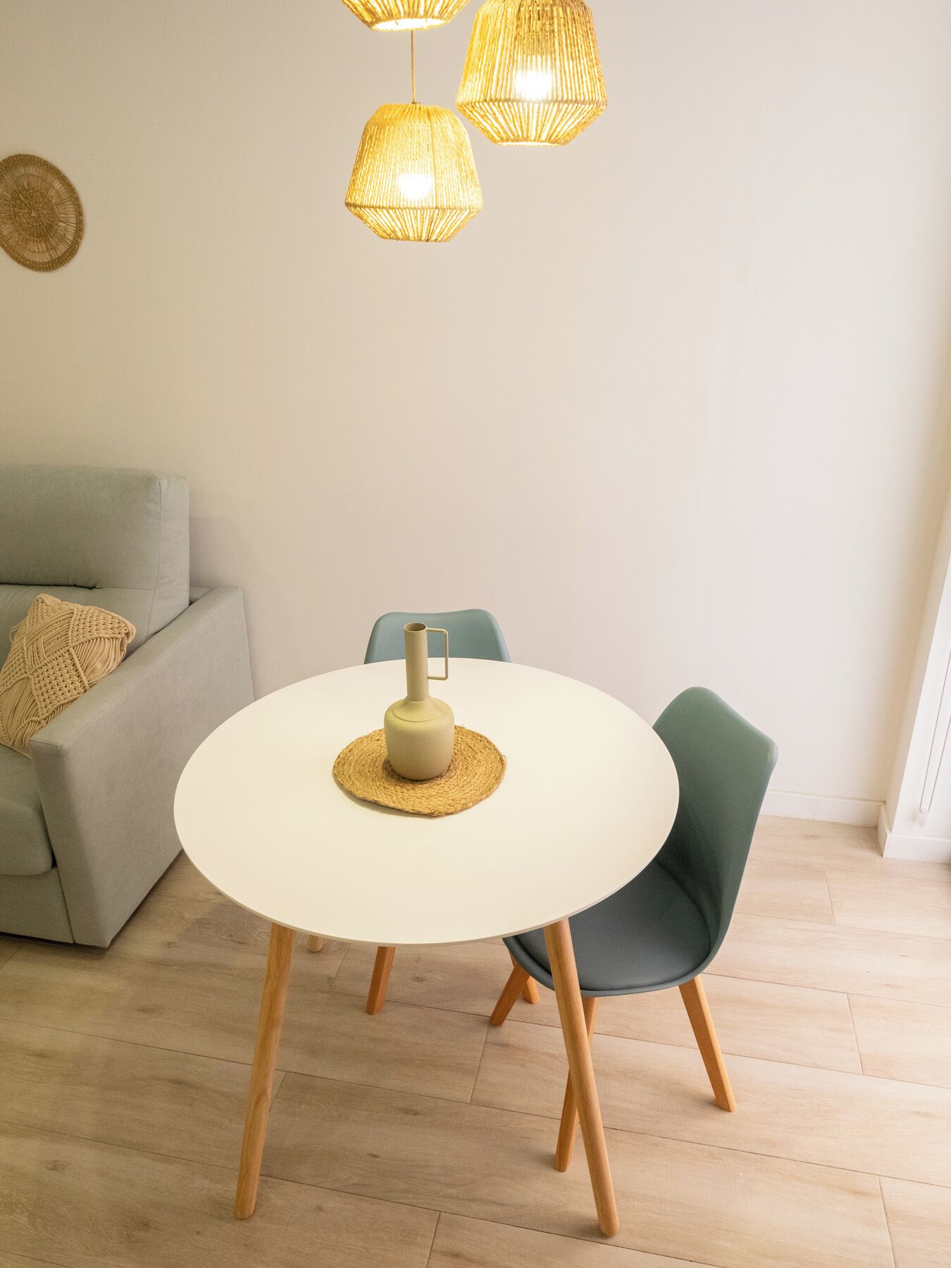 A dining area with a round white table, two chairs, a woven placemat, and a candle holder.