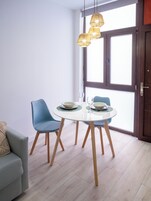 Un comedor moderno con una mesa redonda, sillas azules y una superficie de vidrio. Hay tres lámparas colgantes sobre la mesa.