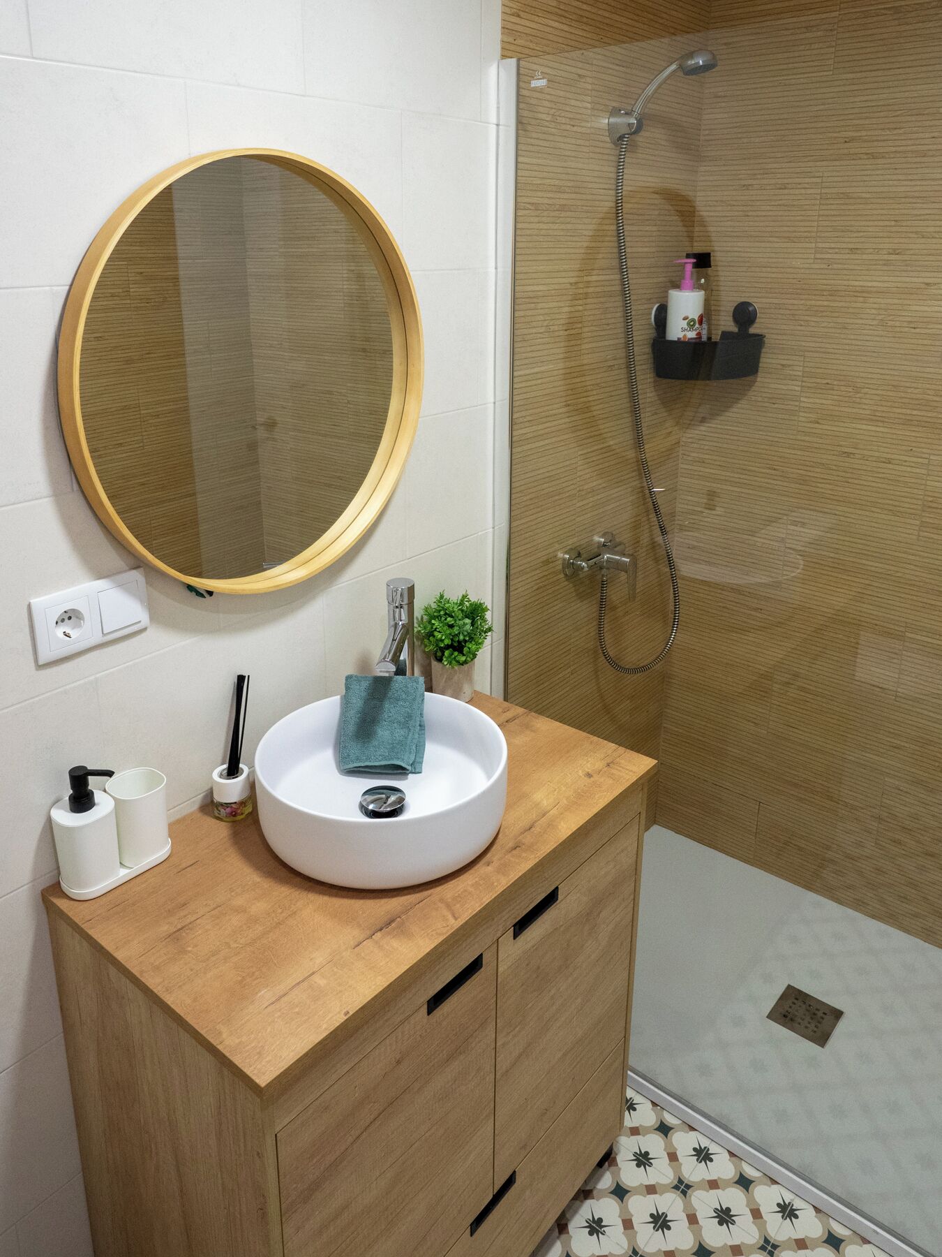 Un baño con un espejo redondo, un lavabo blanco, una planta pequeña y una zona de ducha.