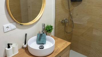 Un baño con un espejo redondo, un lavabo blanco, una planta pequeña y una zona de ducha.