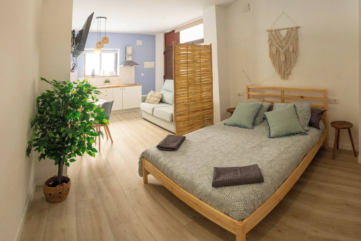 A bedroom with a bed, a bedside table, a hanging macrame wall decoration, a wooden chair, and a potted plant.