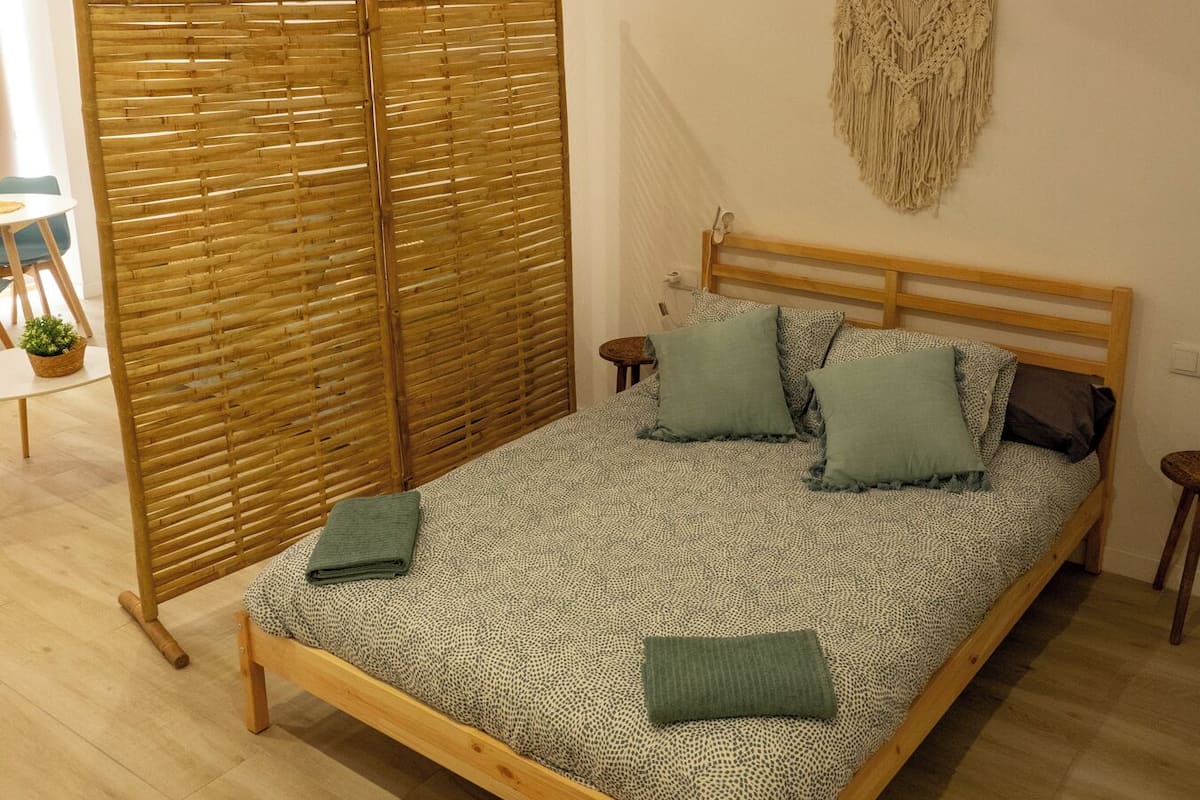 A bedroom with a wooden bed, a ceiling fan, a woven room divider, and a macrame wall hanging.