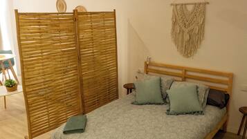 Un dormitorio con una cama de madera, un ventilador de techo, un separador de ambientes tejido y un colgador de pared de macramé.