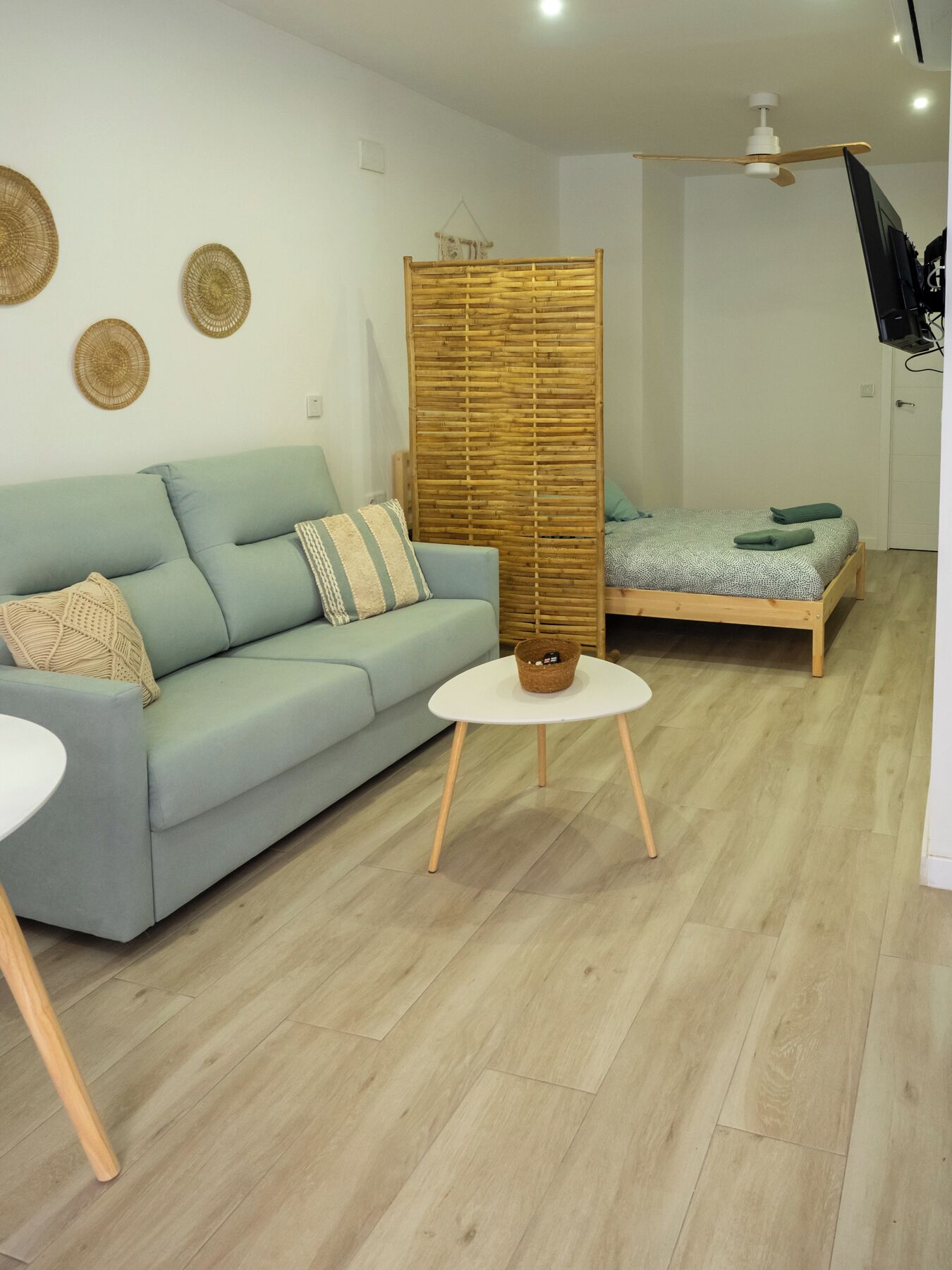 Una sala de estar moderna con un sofá azul claro, una mesa de centro redonda blanca y una cama de madera con colcha verde.