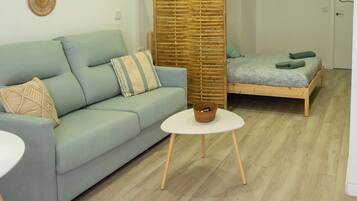 Una sala de estar moderna con un sofá azul claro, una mesa de centro redonda blanca y una cama de madera con colcha verde.
