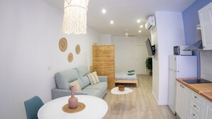 A modern living room with a sofa, a dining table, and a kitchen area with a refrigerator and microwave. - Boho Beach Flats (València)