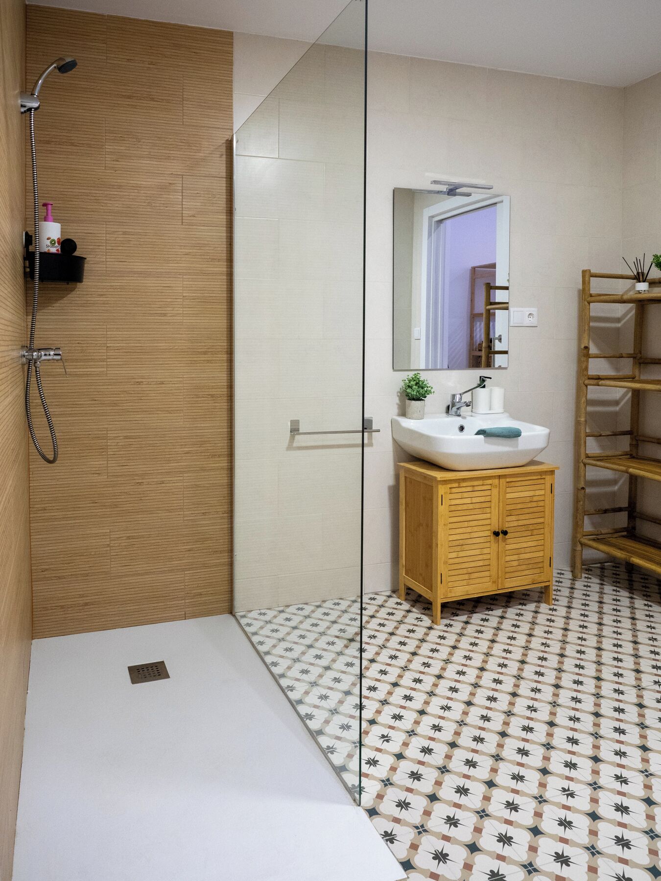 Een moderne badkamer met een douchecabine van glas, een houten wastafelmeubel en een vloer met een patroon.