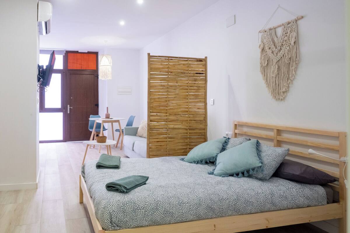 A bedroom with a wooden bed, a wooden headboard, a macrame wall hanging, and a wooden partition.