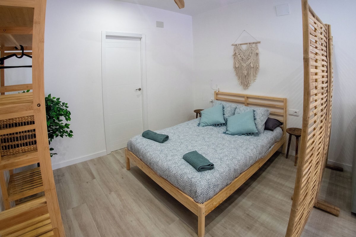 A bedroom with a wooden bed, a ceiling fan, a macrame wall hanging, and a wooden partition.