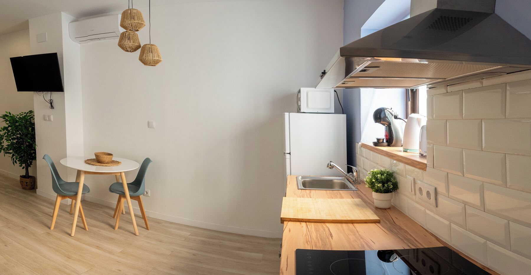 Eine moderne Küche mit einem weißen Kühlschrank, einer Spüle und einer Holz Arbeitsplatte. Es gibt einen Essbereich mit einem runden Tisch und zwei Stühlen.
