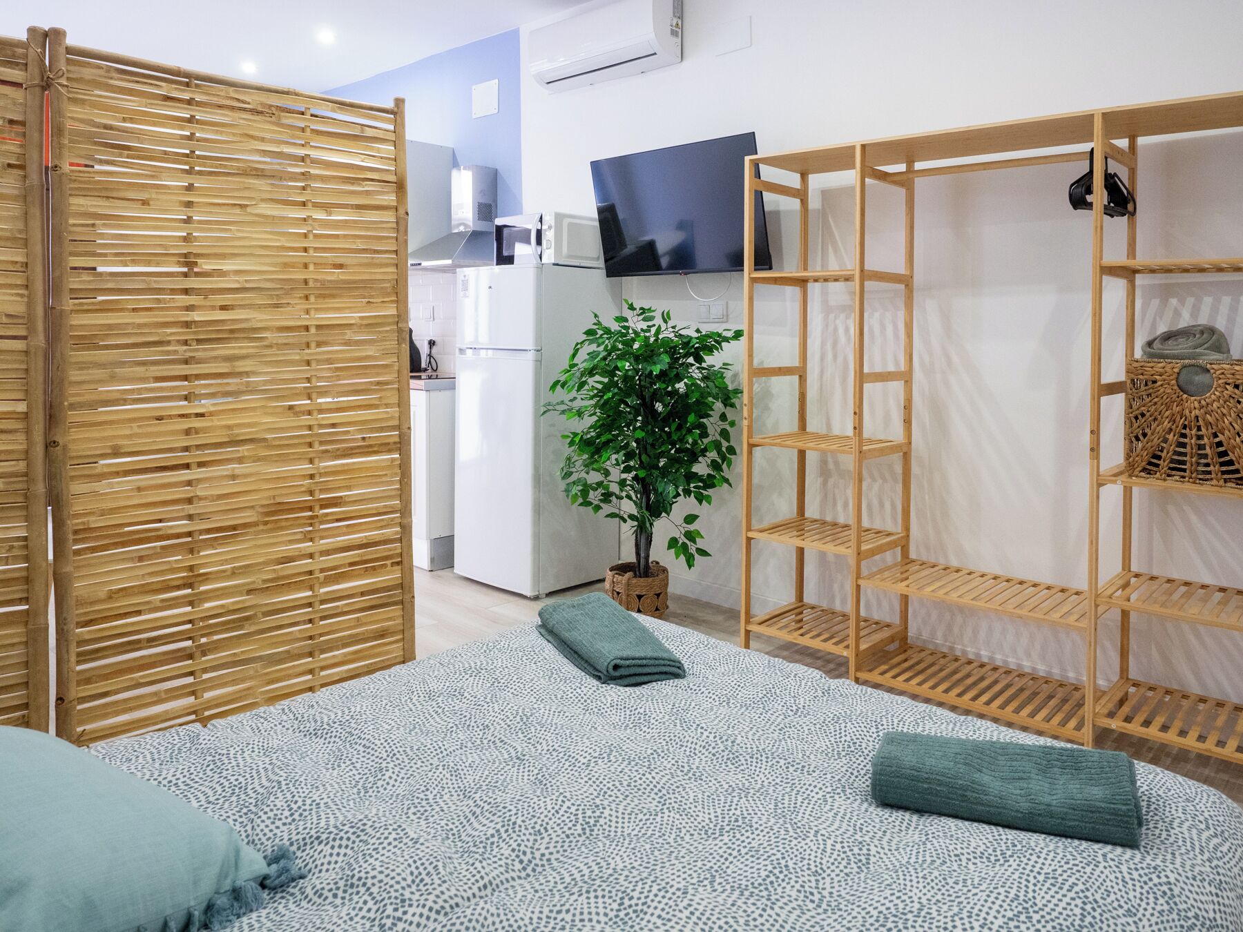 Un espace de vie moderne et compact comprenant un lit, une armoire en bois, un petit coin cuisine et une plante en pot.