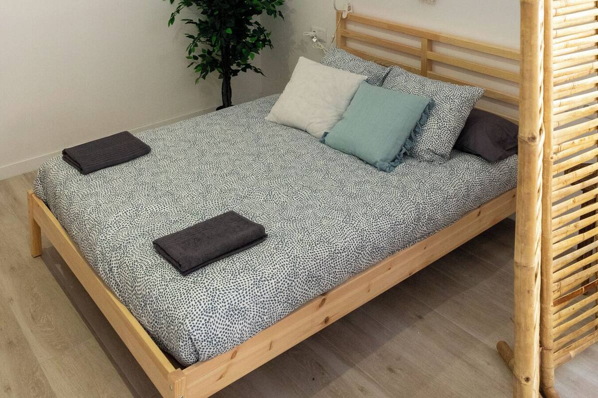 A single bed with a wooden frame, a ceiling fan, a macrame wall hanging, and a small potted plant.
