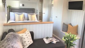 A cozy living area with a sofa, a small table with a magazine, and a plant. - STUNNING SHEPHERDS HUT WITH HOT TUB IN BEAUTIFUL RURAL CHESHIRE, NEAR NANTWICH (Nantwich)