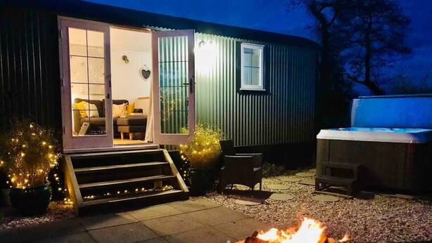 A cozy outdoor area with a fire pit, steps leading to a sliding door entrance, and a patio table. - STUNNING SHEPHERDS HUT WITH HOT TUB IN BEAUTIFUL RURAL CHESHIRE, NEAR NANTWICH (Nantwich)