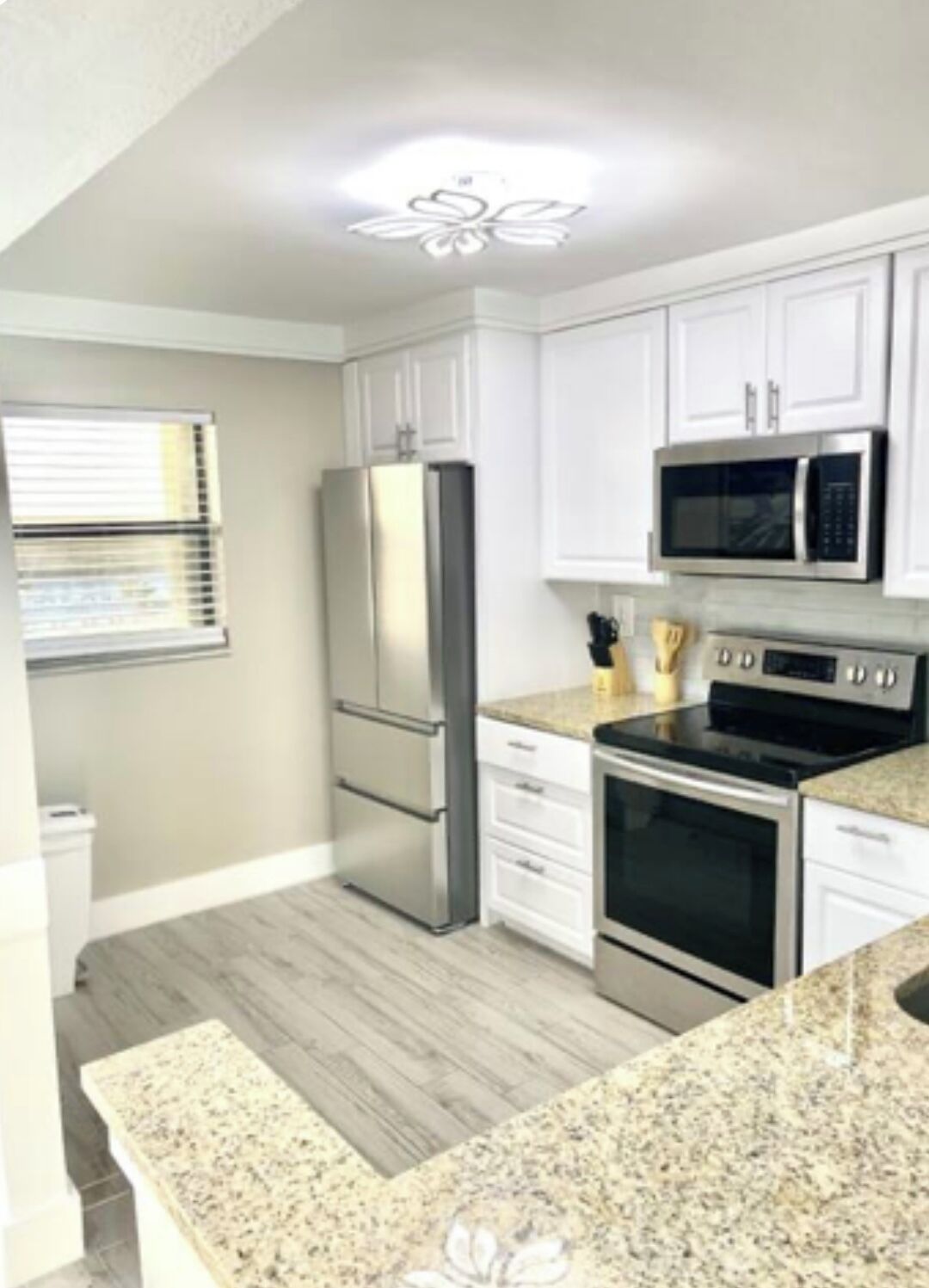 A kitchen with white cabinets, stainless steel appliances, a granite countertop, and a wooden floor.