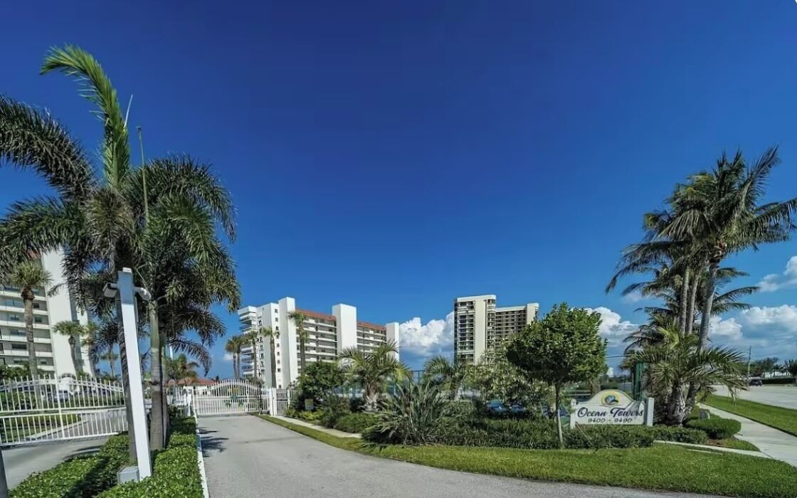 A gated entrance to a hotel complex with palm trees and a clear blue sky.