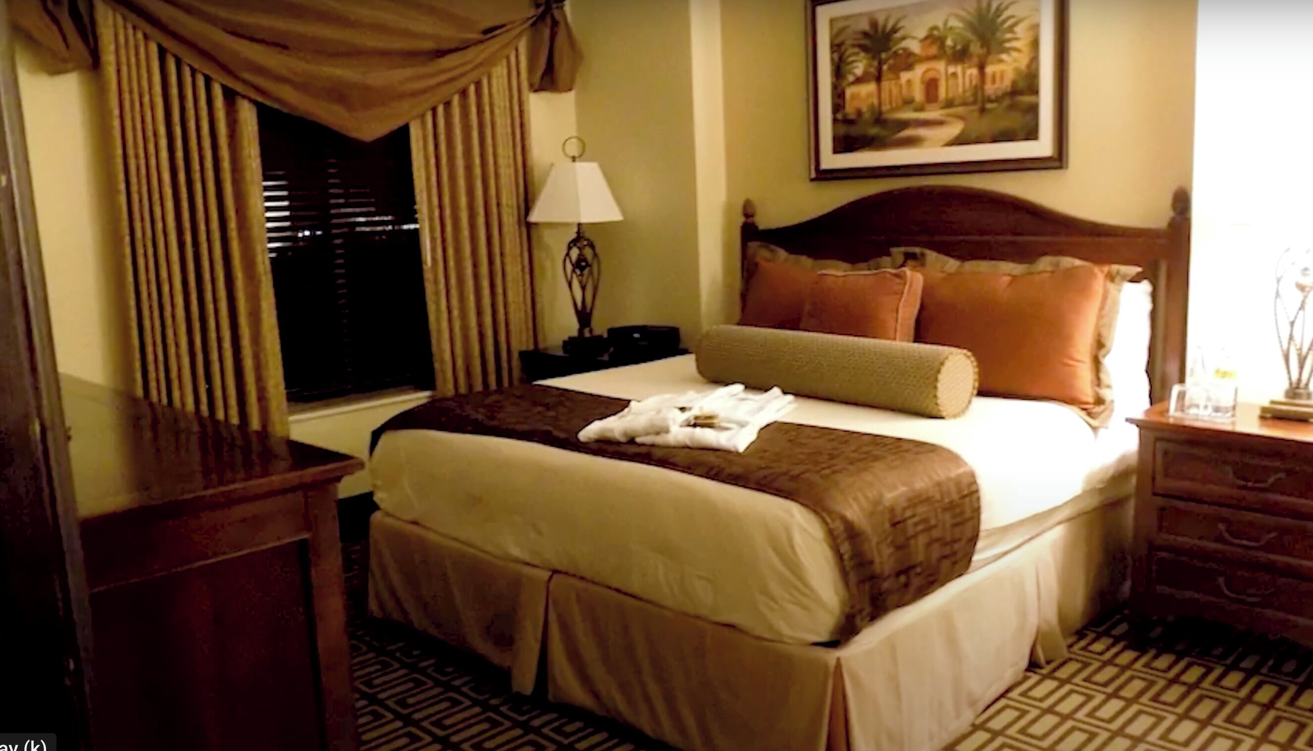 A hotel room with a bed, a nightstand, a lamp, a painting, and a window with curtains.