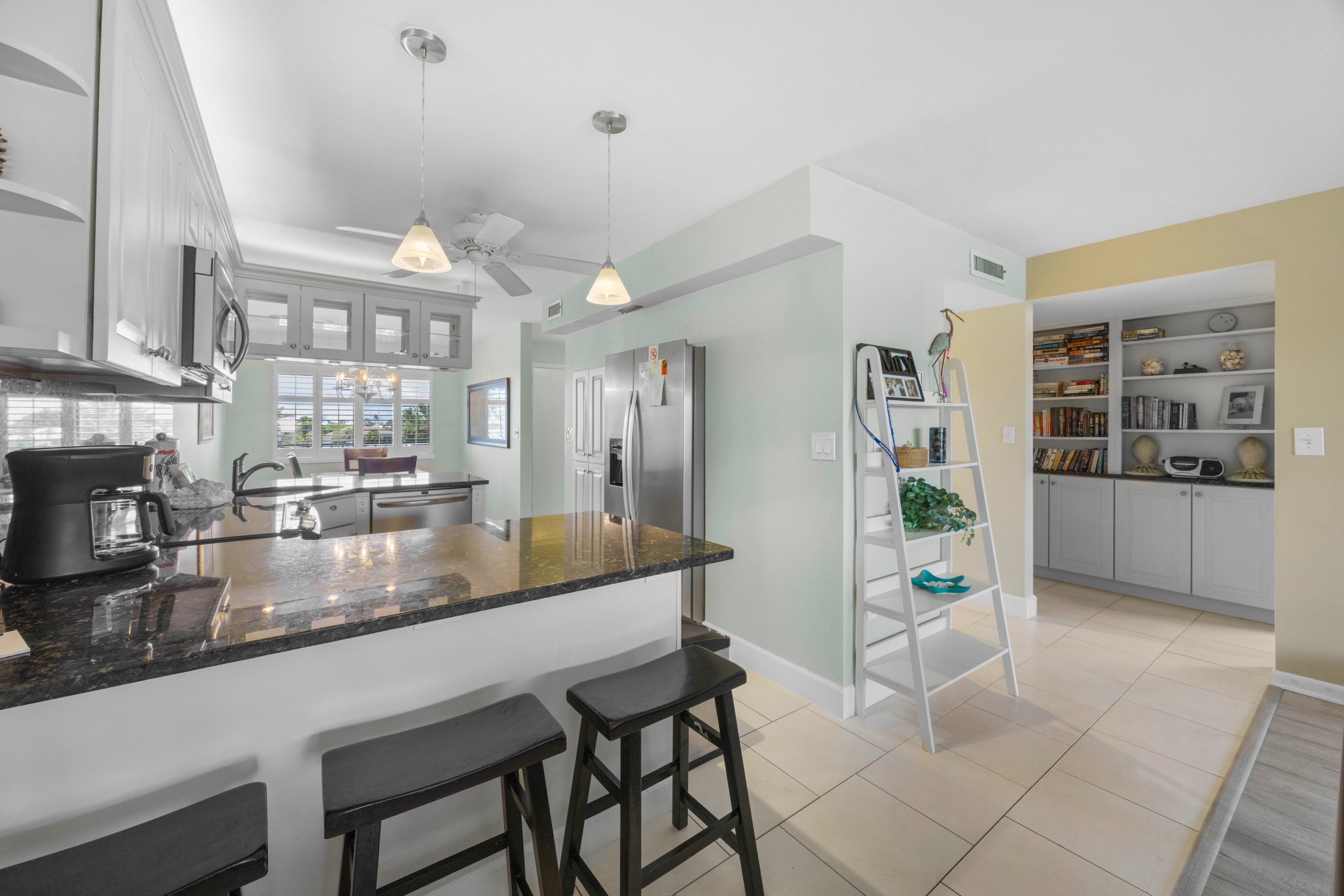 Una cocina moderna con una isla central, taburetes de bar, un refrigerador y una estantería.