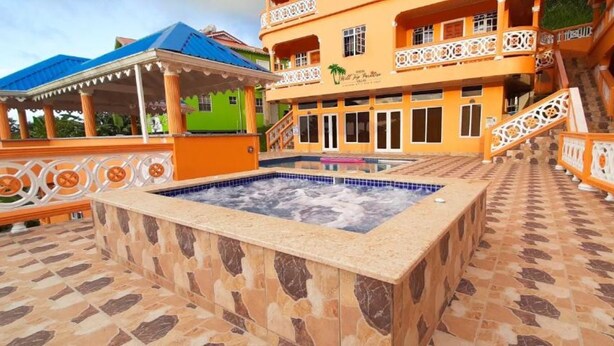 A hot tub area with a tiled floor, a gazebo, and a building with balconies and a pool.