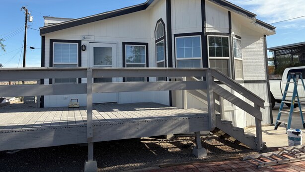 A two-story building with a white exterior and black trim, featuring a front porch with a wooden railing and a small set of stairs leading up to the entrance.