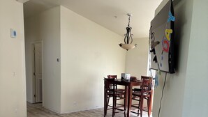 A spacious living room with a wooden floor, a dining area with a table and chairs, and a TV mounted on the wall.