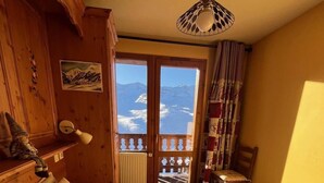 A bedroom with a large bed, wooden wardrobe, a desk with a lamp, and a view of mountains through the door. - 100m from ski slopes, 6th floor, balcony, tv, ski locker, 61m², Val Thorens (Val Thorens)