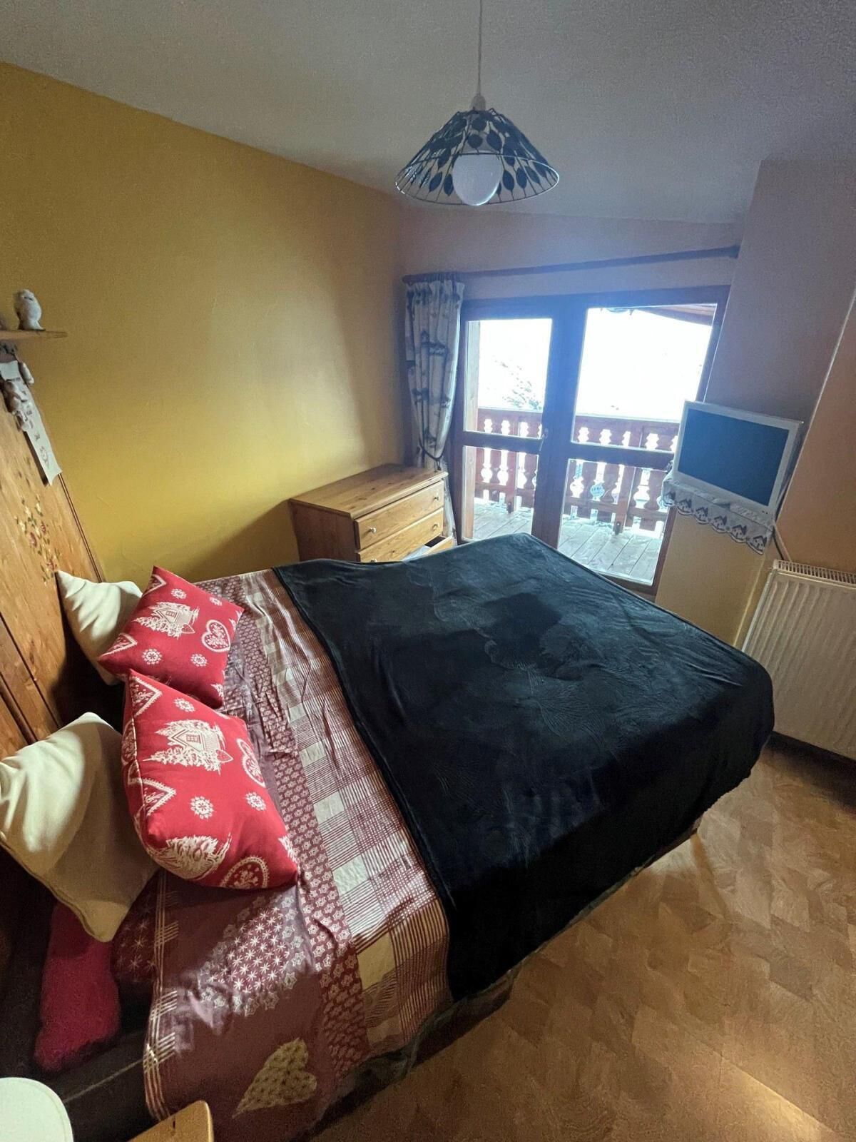 Un dormitorio con cama, cómoda de madera, televisor y balcón con vistas.