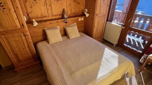 A wooden bedroom with a bed, pillows, a lamp, and a view of a balcony. - 100m from ski slopes, 6th floor, balcony, tv, ski locker, 61m², Val Thorens (Val Thorens)