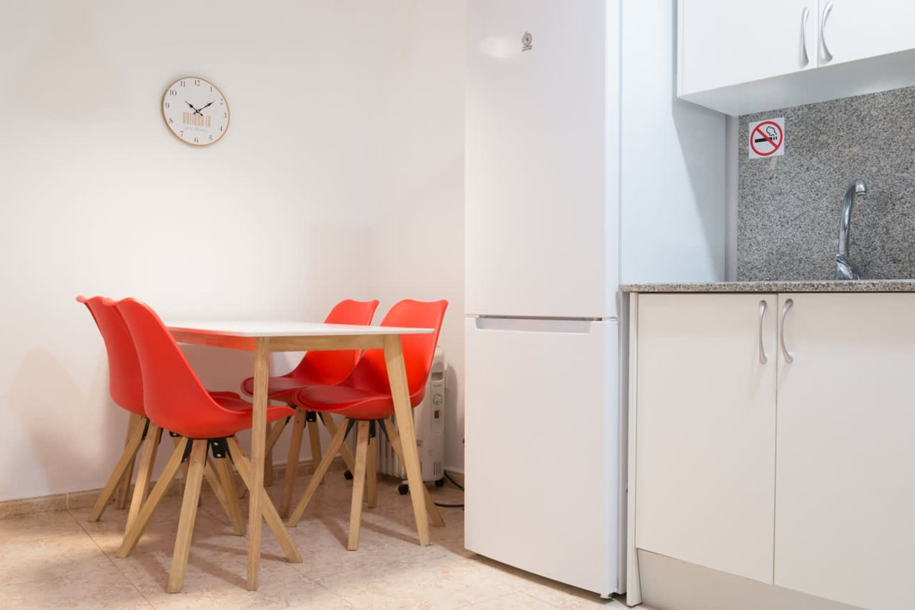 A compact kitchen with white cabinets, a granite countertop, and a clock on the wall.