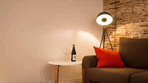 Una sala de estar acogedora con una pared de ladrillo, una mesa redonda con una botella y vasos, y una lámpara de pie moderna.