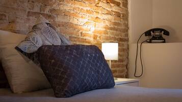 Quarto com parede de tijolos, cama com almofadas estampadas, luminária de cabeceira e telefone antigo.