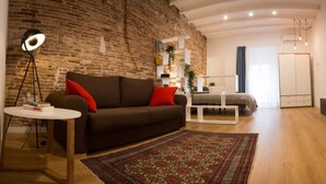 Una sala de estar con pared de ladrillo, un sofá con cojines rojos, una mesa de centro blanca y un armario de madera.