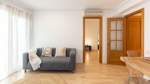 Uma sala de estar moderna com sofá cinzento, piso de madeira e porta de madeira com painéis de vidro jateado.